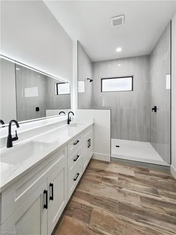 Bathroom featuring double vanity, walk in shower, and light wood-style floors