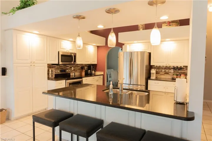 Kitchen with hanging light fixtures, white cabinetry, appliances with stainless steel finishes, and sink