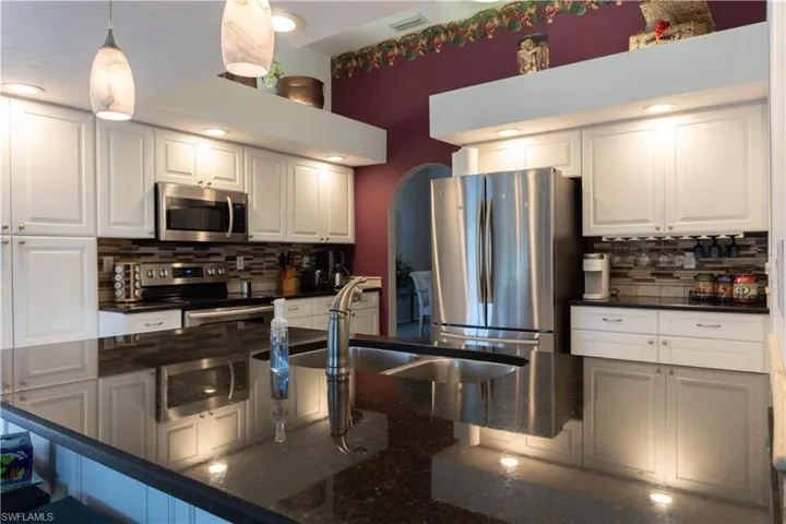 Kitchen with white cabinetry, decorative light fixtures, stainless steel appliances, and dark stone counters