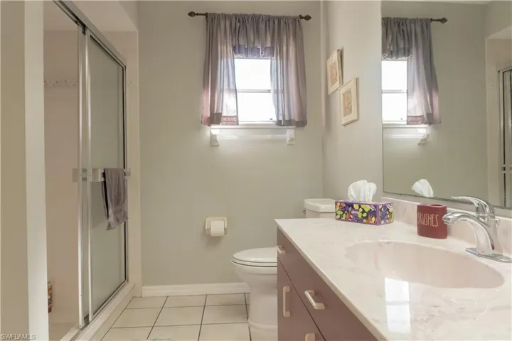 Bathroom featuring tile patterned flooring, toilet, vanity, and a shower with shower door