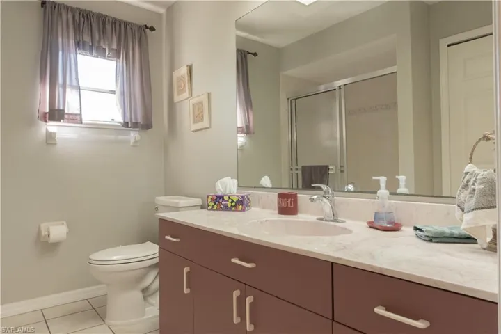 Bathroom featuring tile patterned floors, toilet, a shower with door, and vanity