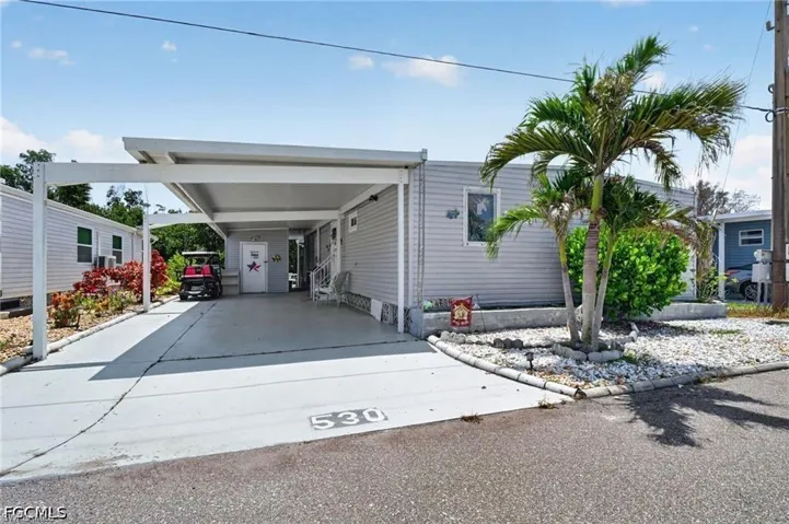 Exterior featuring light-colored horizontal siding, an attached covered carport, a concrete driveway, and a front landscaping bed with decorative rock mulch and a mature palm tree