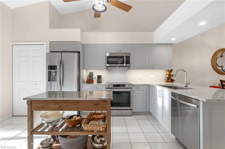 Kitchen featuring light stone counters, stainless steel appliances, sink, lofted ceiling, and light tile patterned flooring