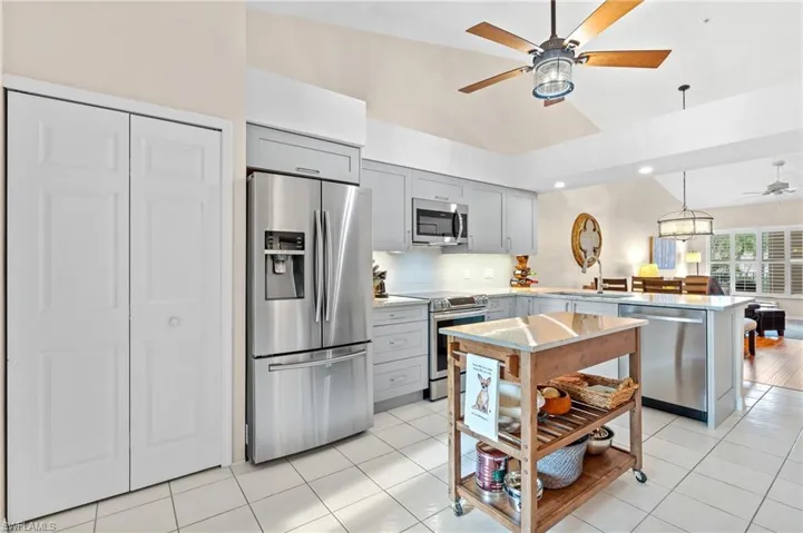 Kitchen with light tile patterned floors, lofted ceiling, stainless steel appliances, and gray cabinetry