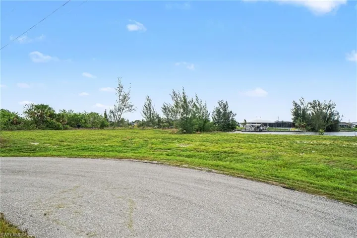 Grassy lot with a paved road frontage and scattered mature trees, featuring a water canal in the background