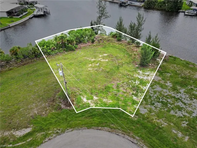 Waterfront lot featuring direct canal access, mature perimeter foliage, and a partially grassed landscape