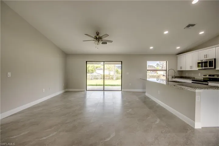 Kitchen with stainless steel appliances, open floor plan, light stone counters, a ceiling fan, and recessed lighting