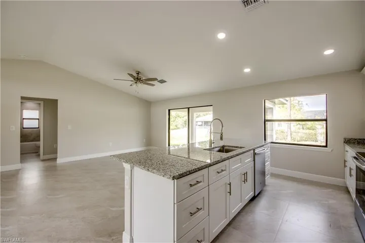 Kitchen with stainless steel appliances, lofted ceiling, a kitchen island with sink, white cabinetry, and light stone counters