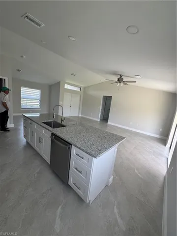 Kitchen featuring dishwashing machine, a kitchen island with sink, open floor plan, white cabinetry, and vaulted ceiling