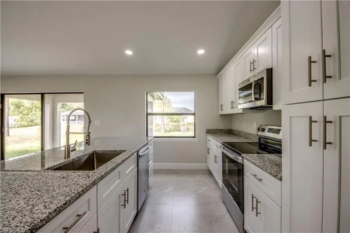 Kitchen with stainless steel appliances, white cabinets, recessed lighting, and light stone counters