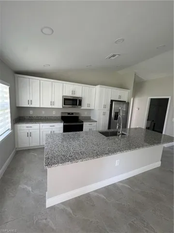 Kitchen featuring range, fridge, lofted ceiling, a spacious island, and white cabinets
