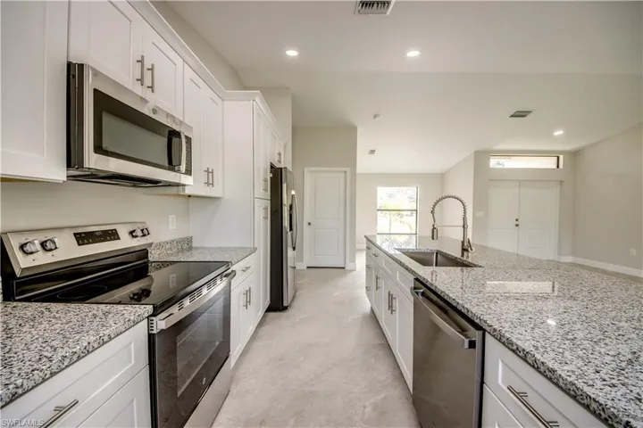 Kitchen with appliances with stainless steel finishes, white cabinetry, light stone countertops, and recessed lighting