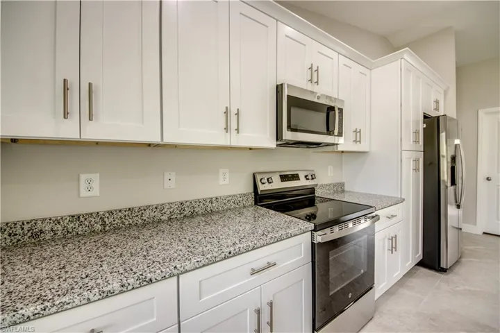 Kitchen featuring stainless steel appliances, white cabinets, light stone countertops, and light tile patterned floors