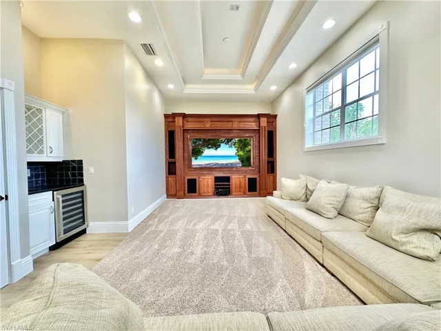 Living room with beverage cooler, recessed lighting, a tray ceiling, bar, and light wood-style floors