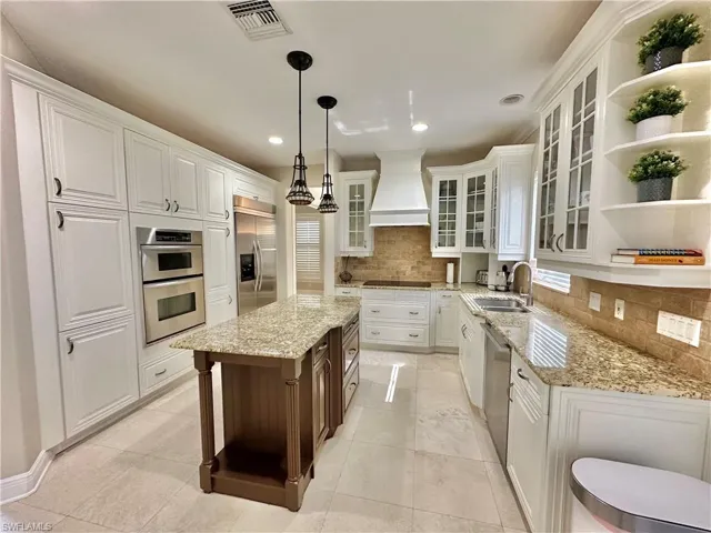 Dual tone kitchen with open shelves, glass insert cabinets, light stone countertops, decorative light fixtures, and two tone color scheme