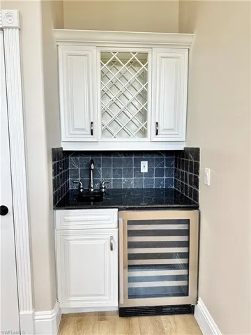 Indoor wet bar featuring dark stone counters, beverage cooler, and white cabinetry