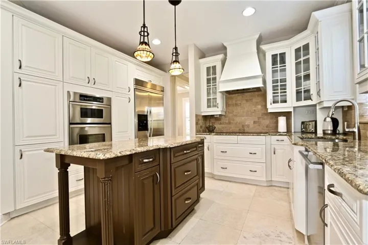 Kitchen featuring two tone color scheme, light stone counters, stainless steel appliances, a center island, and decorative light fixtures