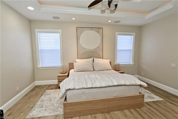 Bedroom with wood finished floors, multiple windows, a tray ceiling, ceiling fan, and crown molding