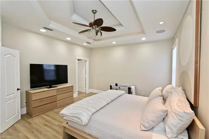 Bedroom with recessed lighting, a ceiling fan, light wood-style floors, ornamental molding, and a raised ceiling