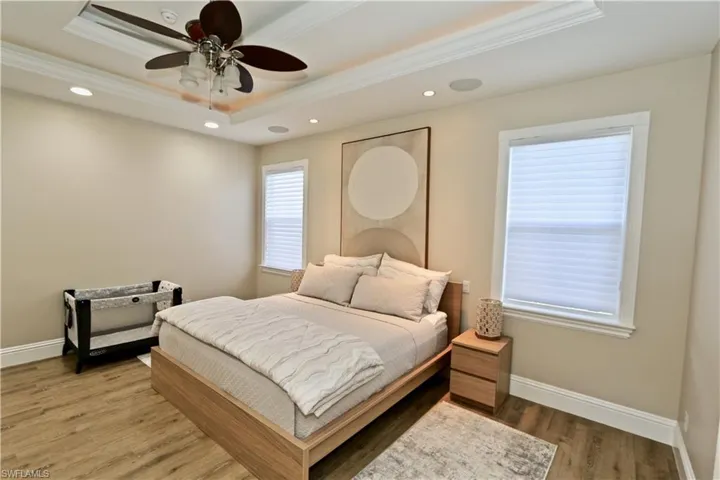 Bedroom with wood finished floors, recessed lighting, crown molding, ceiling fan, and a tray ceiling