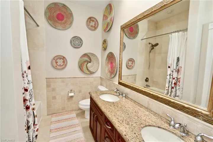 Full bath featuring double vanity, shower / tub combo, tile walls, a wainscoted wall, and light tile patterned flooring
