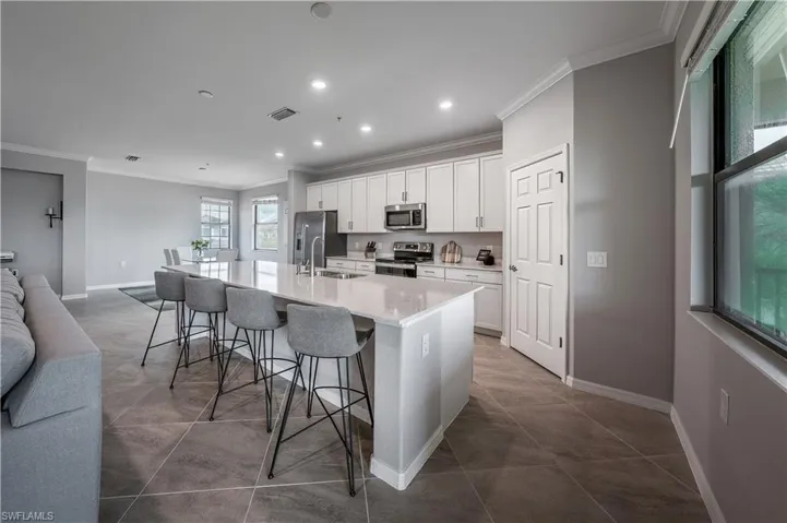 Kitchen with a breakfast bar, white cabinetry, ornamental molding, appliances with stainless steel finishes, and a kitchen island with sink