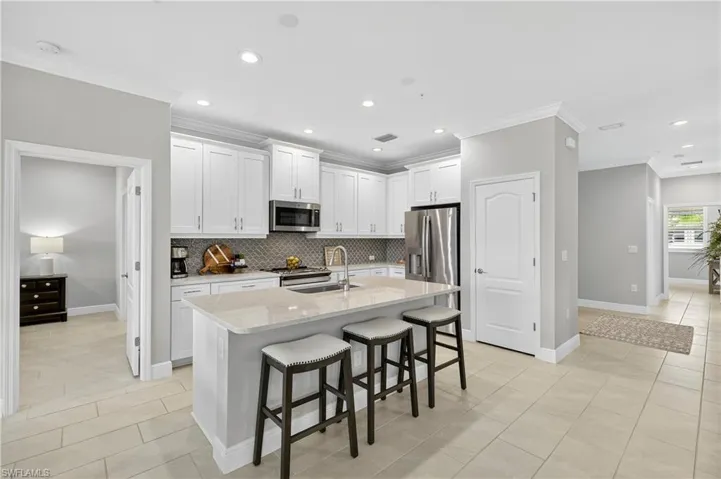 Kitchen with light tile patterned floors, a breakfast bar area, crown molding, light stone countertops, and white cabinets