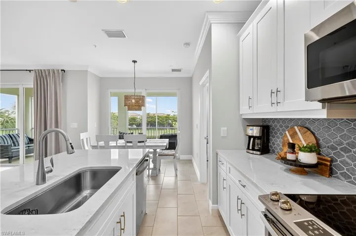 Kitchen with white cabinetry, stainless steel appliances, light stone counters, crown molding, and backsplash