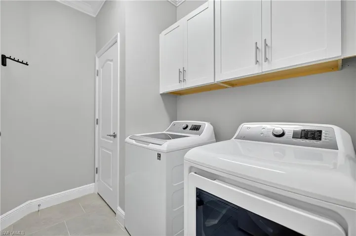 Washroom with light tile patterned floors, separate washer and dryer, cabinet space, and ornamental molding