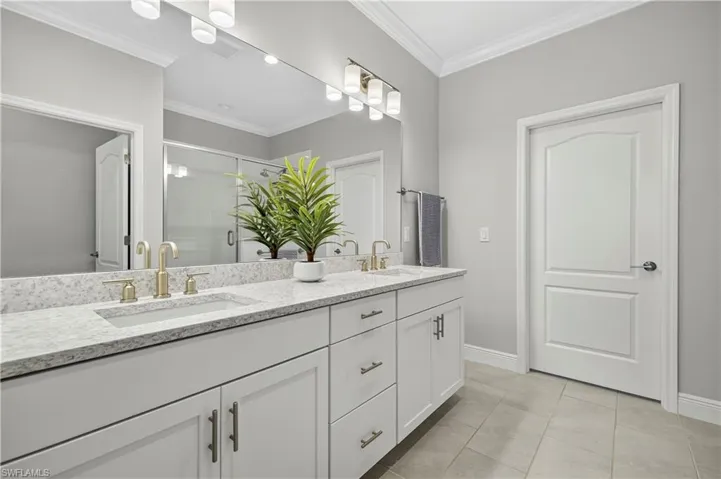 Full bath with double vanity, a shower stall, light tile patterned flooring, and ornamental molding