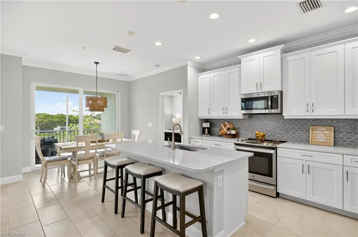 Kitchen featuring ornamental molding, appliances with stainless steel finishes, light stone countertops, light tile patterned floors, and a breakfast bar area