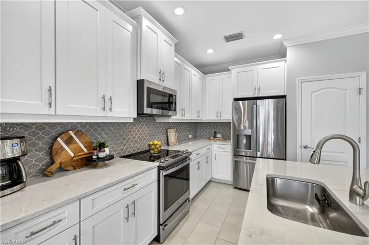 Kitchen with appliances with stainless steel finishes, light stone countertops, white cabinetry, decorative backsplash, and recessed lighting