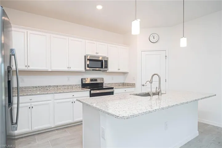 Kitchen with appliances with stainless steel finishes, white cabinetry, a kitchen island with sink, and pendant lighting