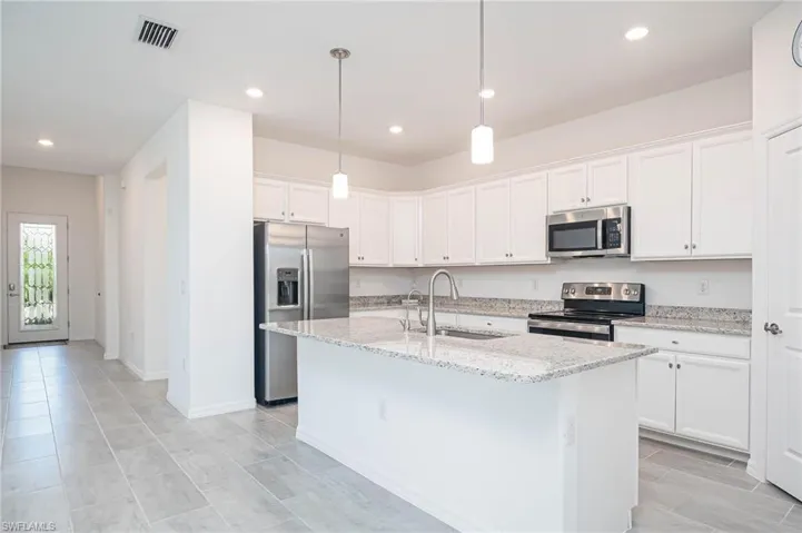 Kitchen featuring light stone counters, stainless steel appliances, a kitchen island with sink, sink, and white cabinets