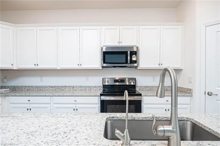 Kitchen with white cabinetry, sink, light stone countertops, and appliances with stainless steel finishes