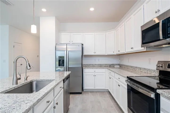 Kitchen with light stone counters, stainless steel appliances, sink, pendant lighting, and white cabinets