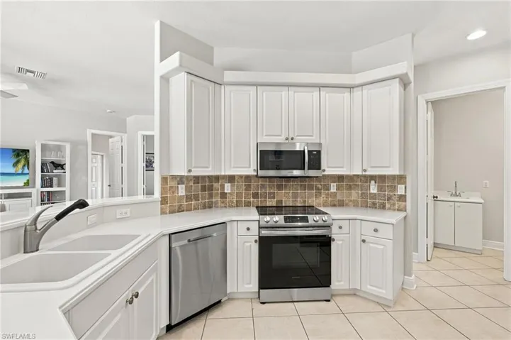 Kitchen featuring white cabinetry, stainless steel appliances, a tile backsplash, solid surface countertops, and a double basin sink