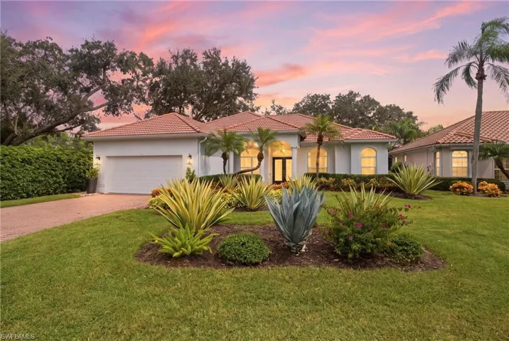 White stucco exterior with a terracotta tile roof, arched windows, and a brick paver driveway