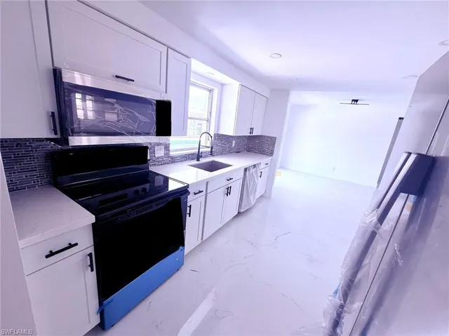 Kitchen with marble finish floor, a sink, backsplash, and appliances with stainless steel finishes