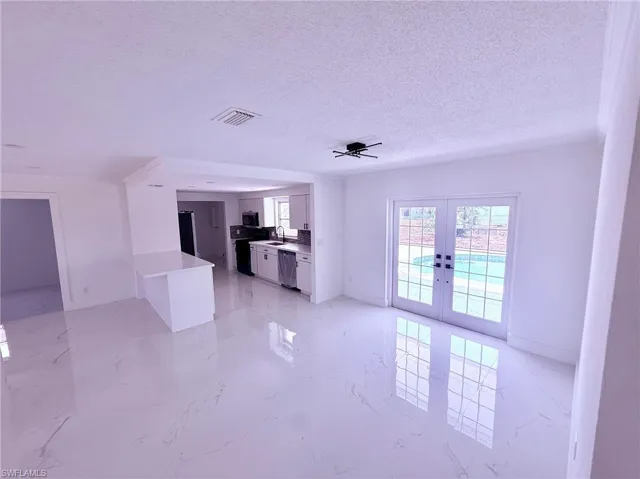 Unfurnished living room featuring french doors, marble finish floor, a sink, and a textured ceiling