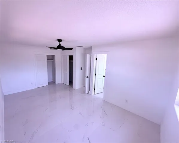 Unfurnished bedroom featuring a ceiling fan, a textured ceiling, multiple closets, marble finish floor, and baseboards