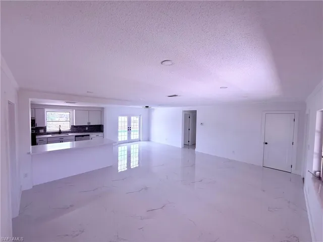 Unfurnished living room with french doors, marble finish floor, a textured ceiling, and a sink