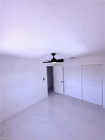 Unfurnished bedroom featuring a textured ceiling, marble finish floor, and a ceiling fan