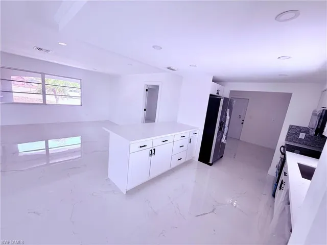 Kitchen with white cabinets, light countertops, visible vents, a peninsula, and stainless steel fridge