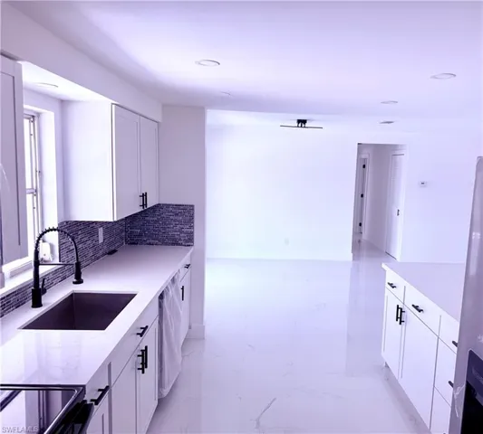 Kitchen featuring a sink, white cabinets, backsplash, light stone countertops, and recessed lighting