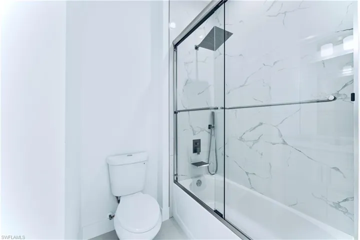 Bathroom with toilet and shower / bath combination with glass door
