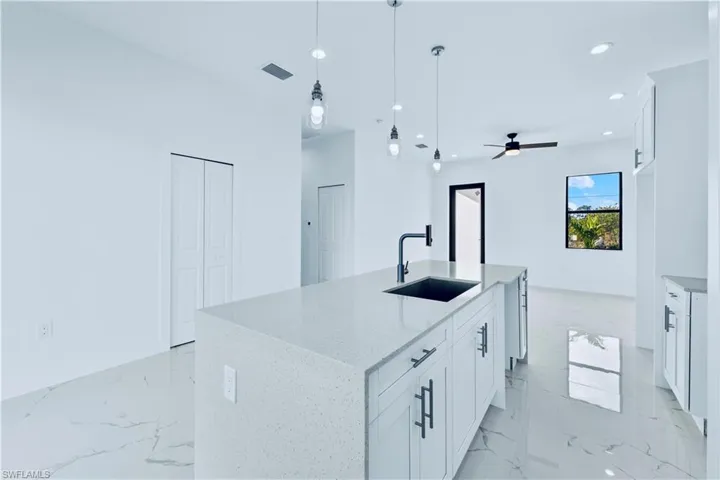 Kitchen featuring light stone countertops, sink, white cabinetry, hanging light fixtures, and an island with sink