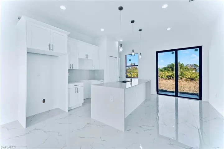 Kitchen with a center island with sink, decorative light fixtures, white cabinets, and sink