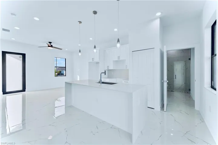 Kitchen featuring ceiling fan, sink, decorative light fixtures, a center island with sink, and white cabinets