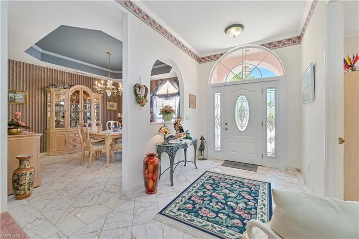 Entrance foyer with crown molding, marble finish floor, baseboards, and an inviting chandelier